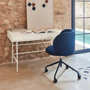 Silla de escritorio giratoria azul frente a un escritorio blanco junto a una pared de piedra