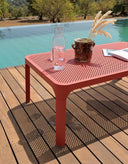 Mesa auxiliar Net 100 en coral en una terraza de madera junto a la piscina – Nardi