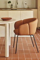 Silla ADD con reposabrazos y patas negras, en polipiel terracota, junto a una mesa redonda – Teulat