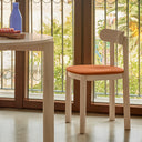 Silla NARA con asiento tapizado en natural claro con asiento terracota, junto a una ventana – Teulat