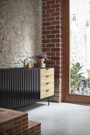 Aparador SIERRA de 159 cm con 2 puertas y 4 cajones, en negro, en un salón con pared de ladrillo – Teulat