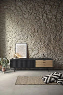 Mueble TV SIERRA de 180 cm con 2 puertas y 3 cajones, en negro, en un salón con pared de piedra – Teulat